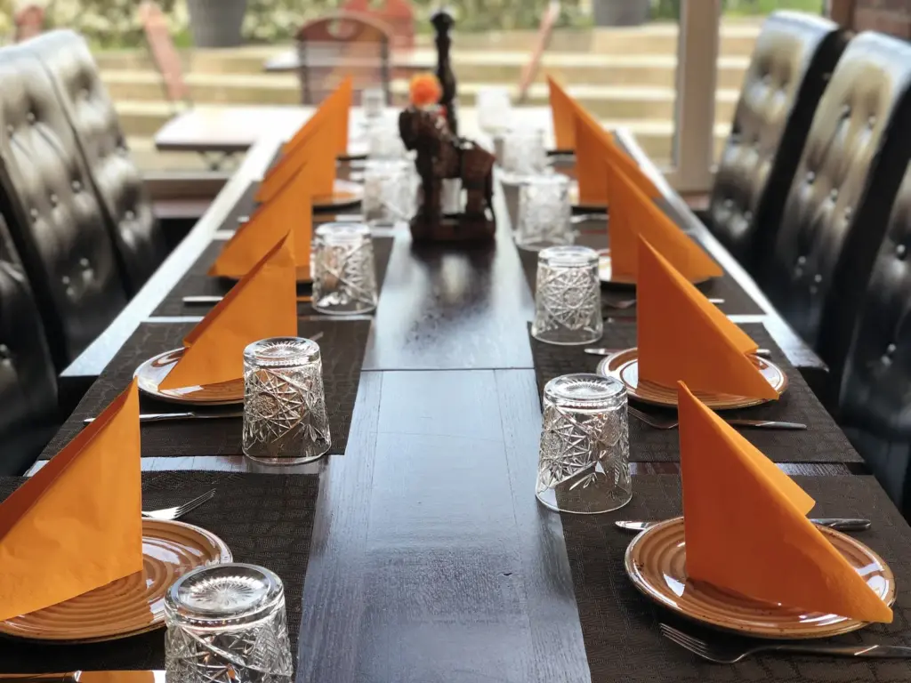Lange gedeckte Tafel mit orangefarbenen Servietten und Kristallgläsern im TROY Restaurant Hennef