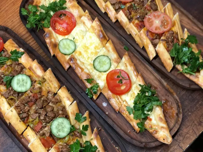 Drei Pide auf Holzbrettern – mit Fleischwürfeln und mit Käse, garniert mit Tomate, Gurke und Petersilie – TROY Restaurant Hennef